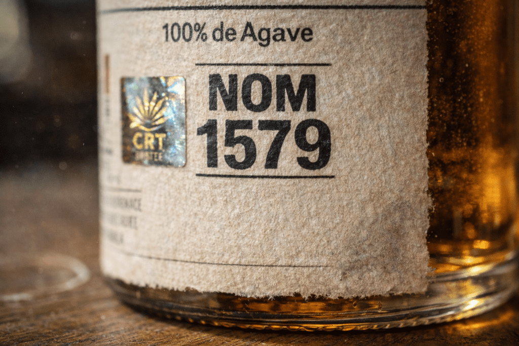 Close-up of tequila bottle label showing NOM number certification mark and 100% agave designation for authenticity verification